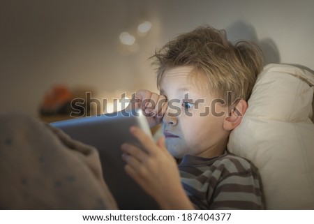 little tired boy at expressive face using a digital tablet in bed