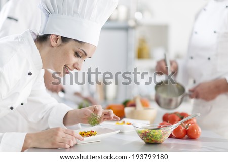 closeup on a  female chef preparing a dish her team in the background