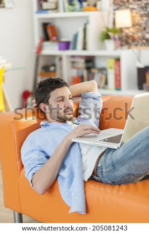 young student lying on a couch surfing  the web  on his laptop