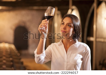 Professional winemaker female tasting a glass of red wine in his traditional cellar surrounded by wooden barrels