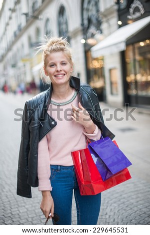 beautiful trendy young woman with shopping bags walks in the streets, a black leather jacket on her shoulders
