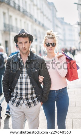 a trendy young couple walks in the city, the young woman has shopping bags at her arm