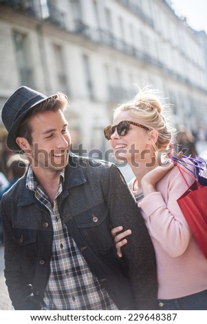 a trendy  young couple laughs in the city, the young woman has shopping bags at her arm