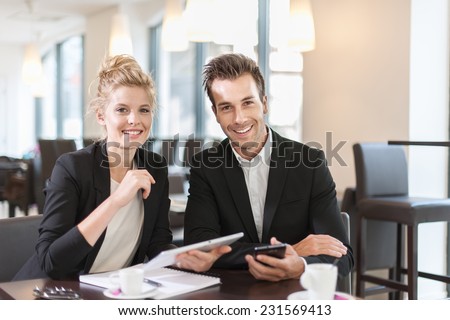 Couple of colleague  wearing suits, sitting at a table and using a digital tablet in a meeting