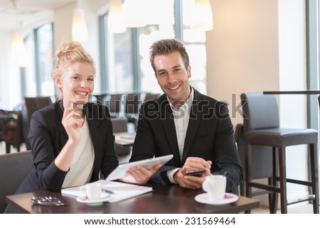 Couple of colleague  wearing suits, sitting at a table and using a digital tablet in a meeting