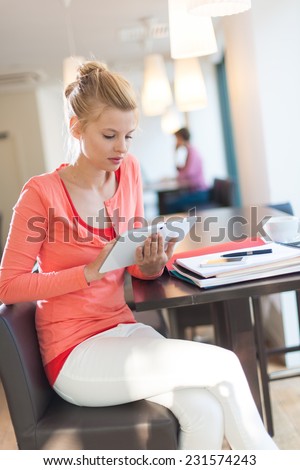smiling young female student sitting in a cafe to work, using a digital tablet