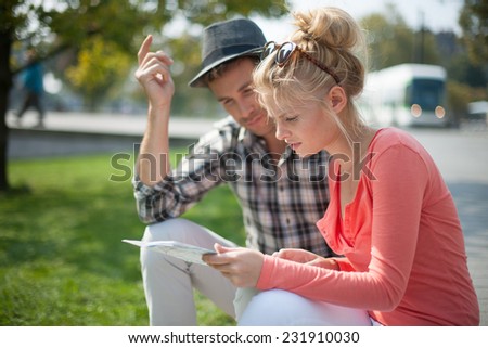 young tourist couple looking at a map in a European city, man wears hat,  the woman wears sunglasses, a bus at the background