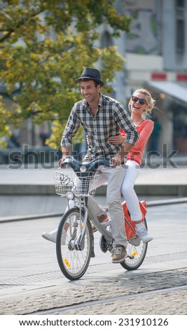 young couple in vacation having fun on a rental bike in the city, in summer