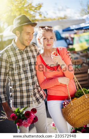 a young couple walking on a market on a sunny morning, the young woman carries a basket with fruit and vegetables