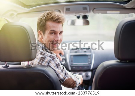handsome man looking at camera sitting in a car, view from rear seat