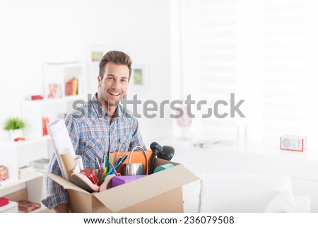 portrait of an handsome man moving in  a new apartment and carrying a box with various objects
