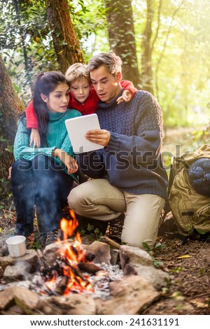 in the evening, cheerful family using a digital tablet, heats up near a campfire in the woods