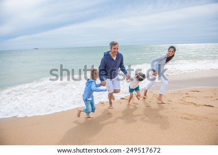 A four people family is playing in the sea waves, the parents and their two children are holding hands while running back from the sea waves