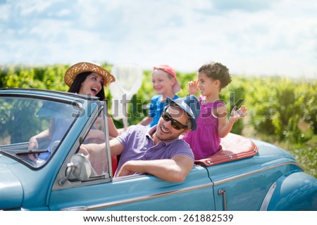A lovely family is going on vacation in a convertible retro car. they drive on a country road on a sunny day
