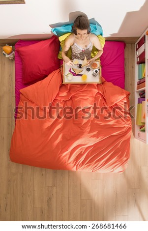 top view, single young woman, having breakfast in bed by a sunny morning, the bedding has bright colors