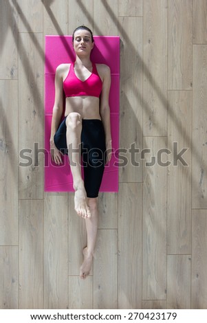 Top view, young woman doing stretching exercises on a pink carpet, window casts graphics shadows on the floor
