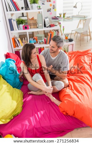 a glamour couple in pajamas, sitting in bright colors's bed, man has gray hair, their apartment is modern and bright