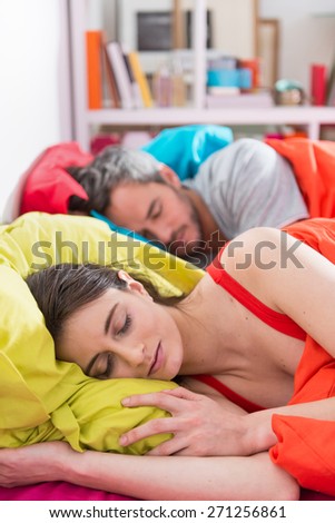 Handsome couple sleeps in bed on bright colored pillows, bedding is bright color,their sunny apartment is modern and bright