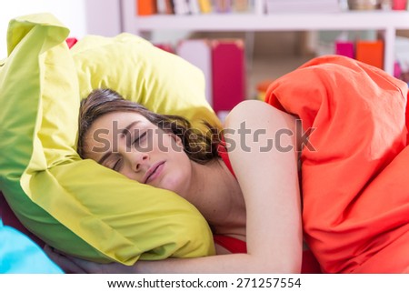 a gorgeous young woman sleeps in bed,  colored pillow in her arms,bedding is bright color, her sunny apartment is modern and bright