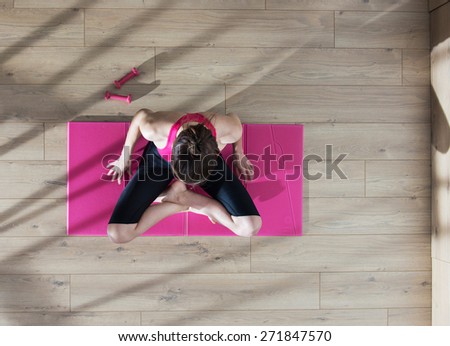Top view, young woman doing stretching exercises on a pink carpet, window casts graphics shadows on the floor