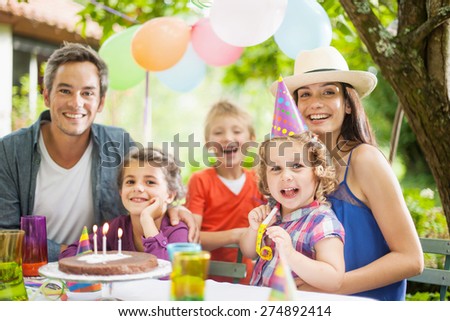 garden party with family for little girl\'s birthday, the whole family looking at camera, the garden is decorated with balloons and colors are bright