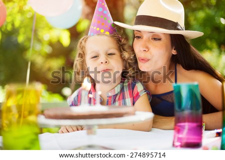 garden party with family for little girl\'s birthday, children blows out the candles on the cake, the garden is decorated with balloons and colors are bright