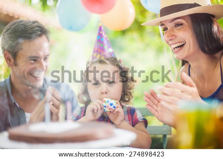 garden party with family for little girl\'s birthday, girl blowing out the candles on the cake, the garden is decorated with balloons and colors are bright