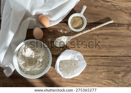 top view, ingredients to make a cake on a wooden table, a bowl flour, sugar, eggs and napkin