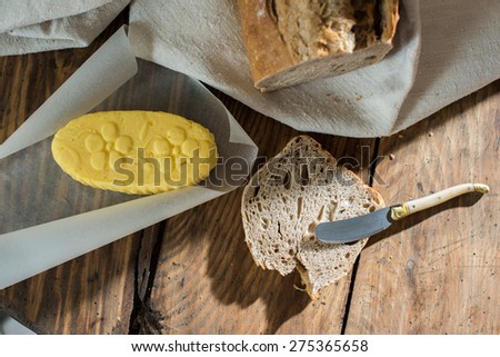 Top view, rustic bread wrapped in a linen cloth and butter on a wooden table, slice of bread and knife