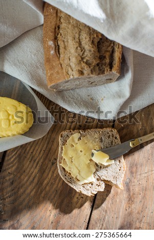 Top view, rustic bread wrapped in a linen cloth and butter on a wooden table, slice of bread and knife