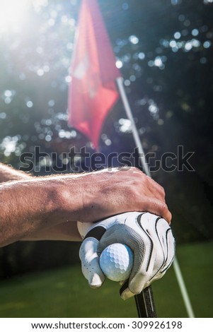 Backlit shoot with flare. Close up of golfer hands, with white glove, holding a ball, crossed on the top of the club. Focus on the hands and the ball.