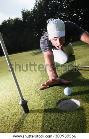 Golfer stunned because he missed his last swing Handsome golfer lying down on the green, hands on the ground Wide angle view with a beautiful forest in the background