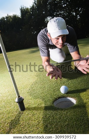 Golfer stunned because he missed his last swing Handsome golfer lying down on the green, hands on the ground Wide angle view with a beautiful forest in the background