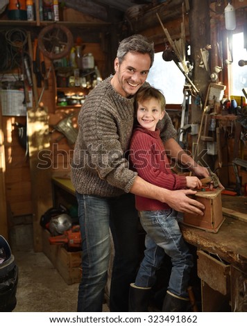 Portrait of a father and his son working together on a birdhouse in a traditional wooden workshop They are looking at camera the son is holding a hammer while his grey hair father is holding the house