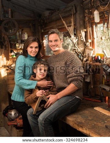 Portrait of family working a in rustic wooden workshop Mother, father and daughter are sitting on the wooden table holding a birdhouse. They are smiling, and looking at camera