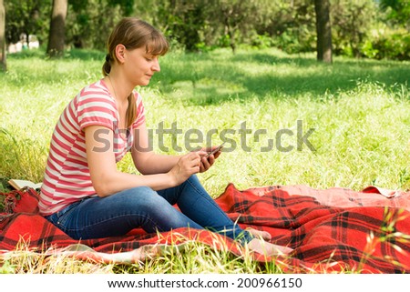 young woman sitting under a tree with a phone in the park