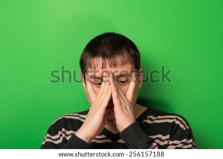 man covered his face with his hand on a green background