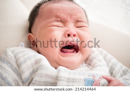 crying asian newborn baby lying on bed