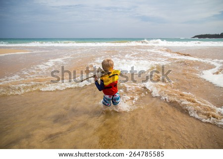 Small blond haired boy is a life vest playing in the shallow ocean water