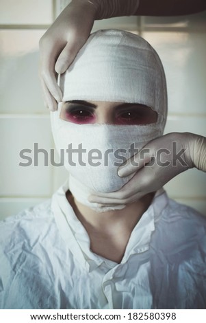 Hands in surgical gloves is holding bandaged head