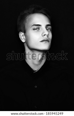 Trendy young boy with blue eyes in a black shirt posing on a black background, black and white