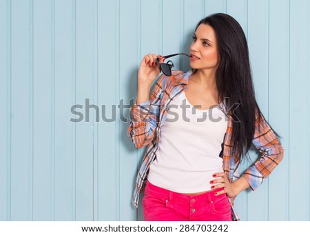Summer, fashion and people concept - brunette in shirt posing in sunglasses against colorful wall background in the city, smiles sweetly looking sideways, copy space, street fashion photo.