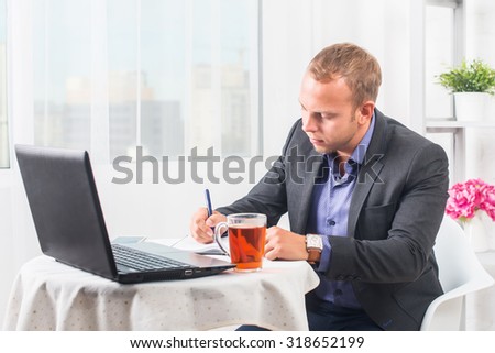 Businessman in office sitting at table with a laptop writes concentration