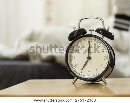 Retro black alarm clock show 7 o\'clock in the morning for wake up.Background is a bedroom.