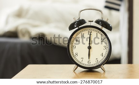 Retro black alarm clock show 6 o\'clock in the morning for wake up.Background is a bedroom.
