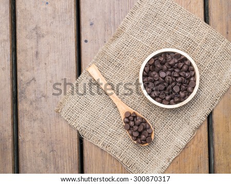 Top view -  Chocolate chips in wooden spoon and bowl on  burlap hessian sacking