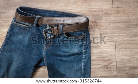 Top view of blue jeans with leather belt on the wooden background ( Composition and space for text )