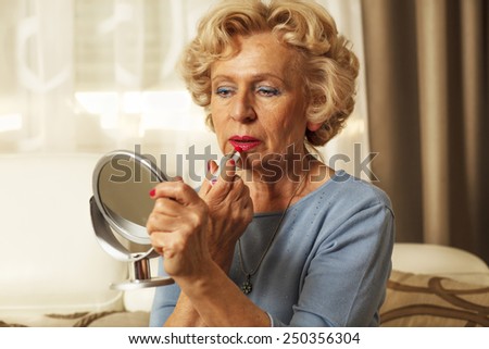 Elderly woman applied lipstick and looked in the mirror.