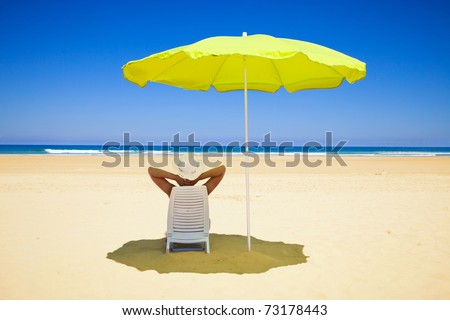 woman resting under umbrella facing the seaside in a deserted beach with deep blue sky