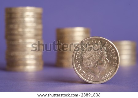 One pound coin in front of stacks of several coins against purple background